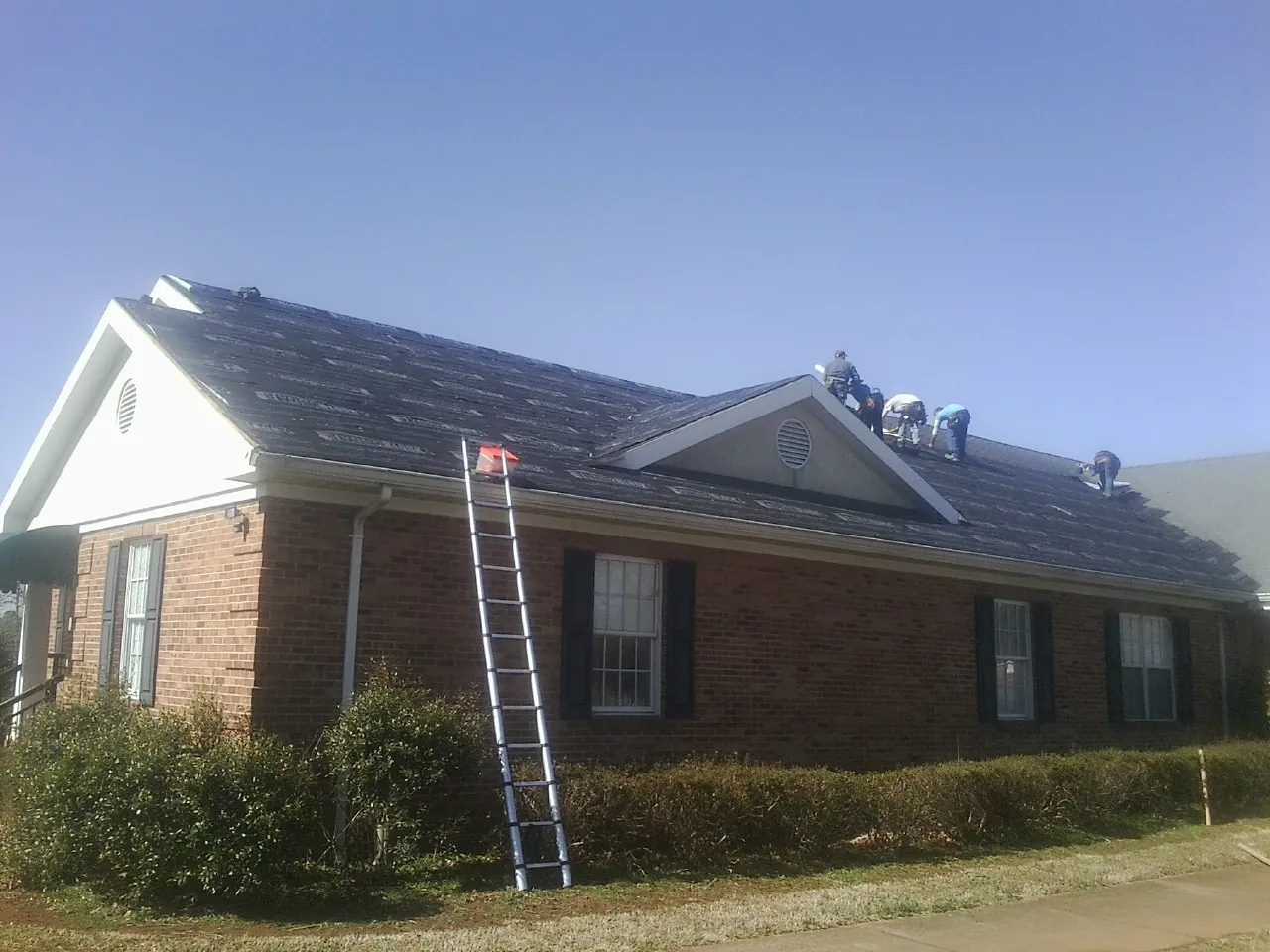 Crew tearing shingles off a brick ranch roof with a ladder set — Metal Roof Repair work by our crew in Palatine