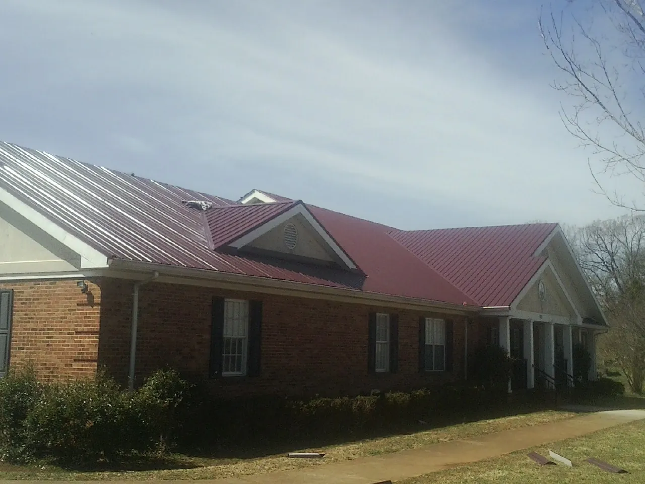 Red metal roof with gabled entries on a long brick building, from a Hail Damage Roof Repair job in Palatine