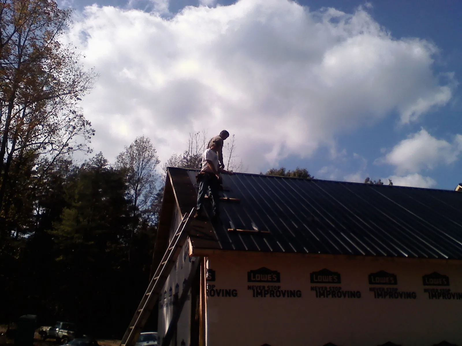 Roofer fastening dark metal panels high against a cloudy sky, from a Roof Inspection job in Palatine